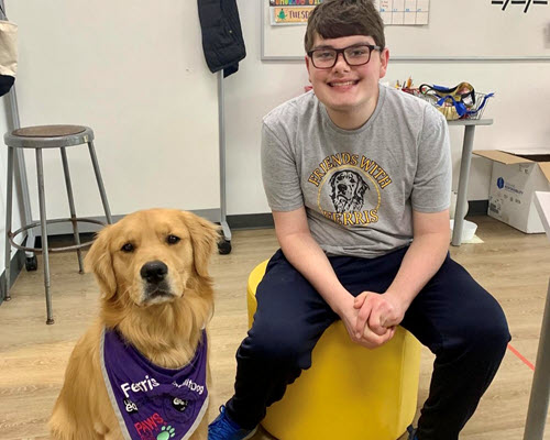 student sitting next to a golden retriever dog