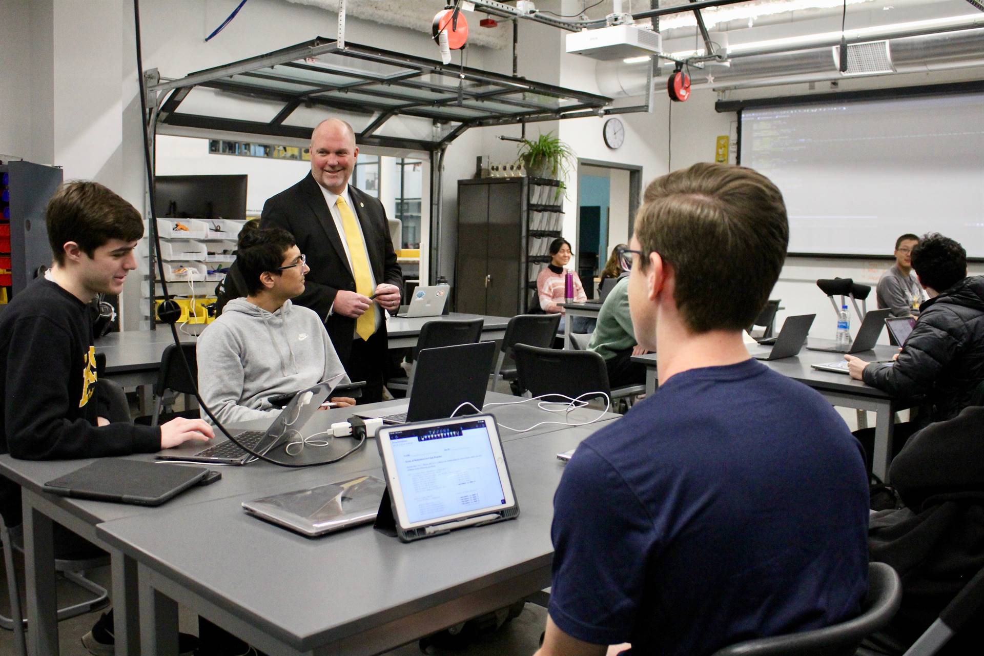 Dr. Robert Hunt (standing) interacting with three students sitting at a table in a computer science 