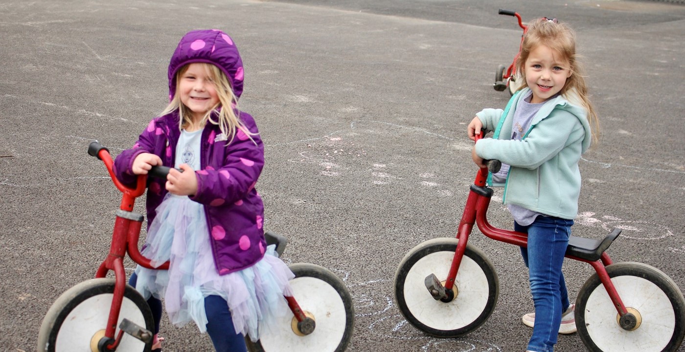 Two children smiling for a photo while on balance bikes