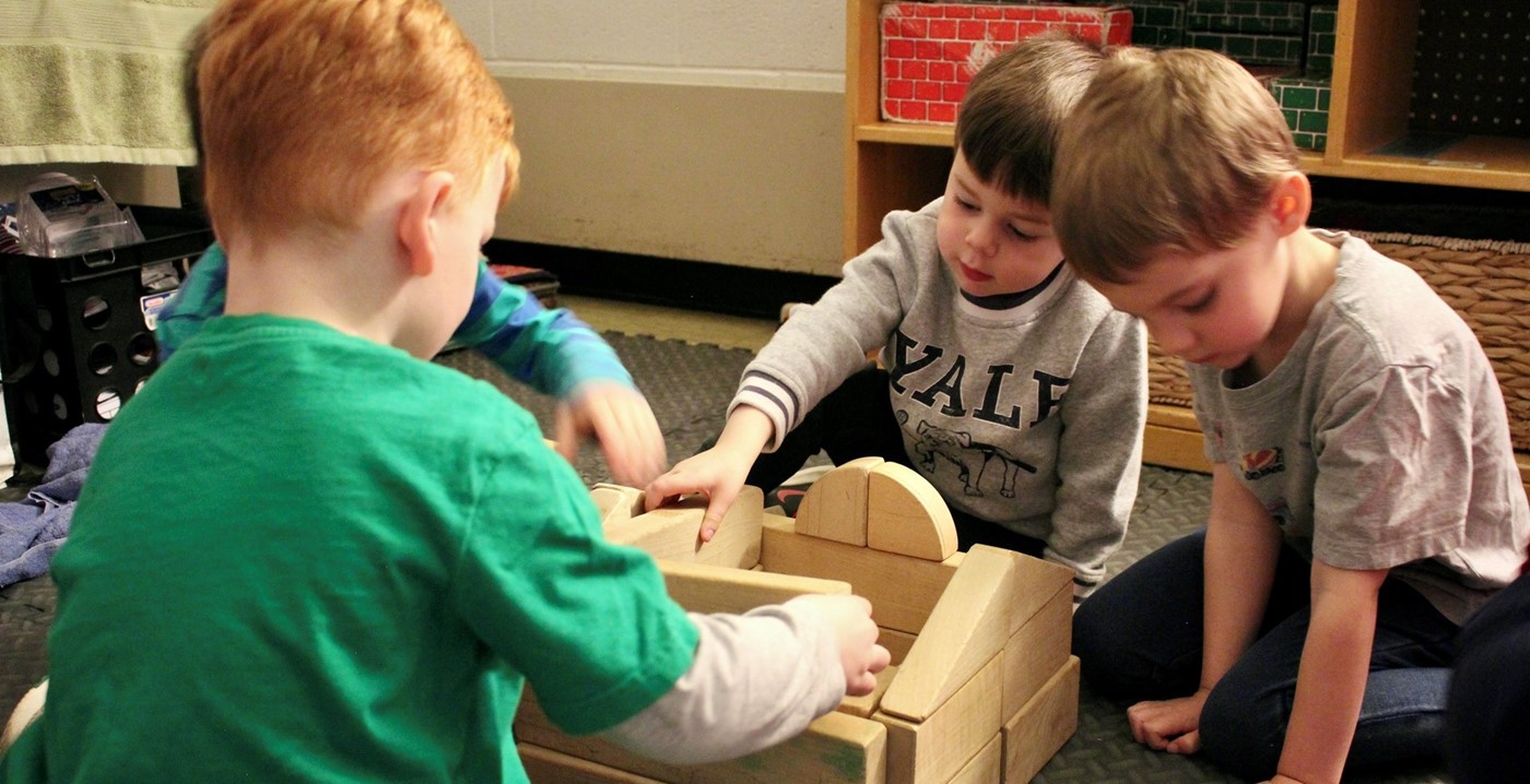 Children sitting on the floor building a structure with wooden blocks