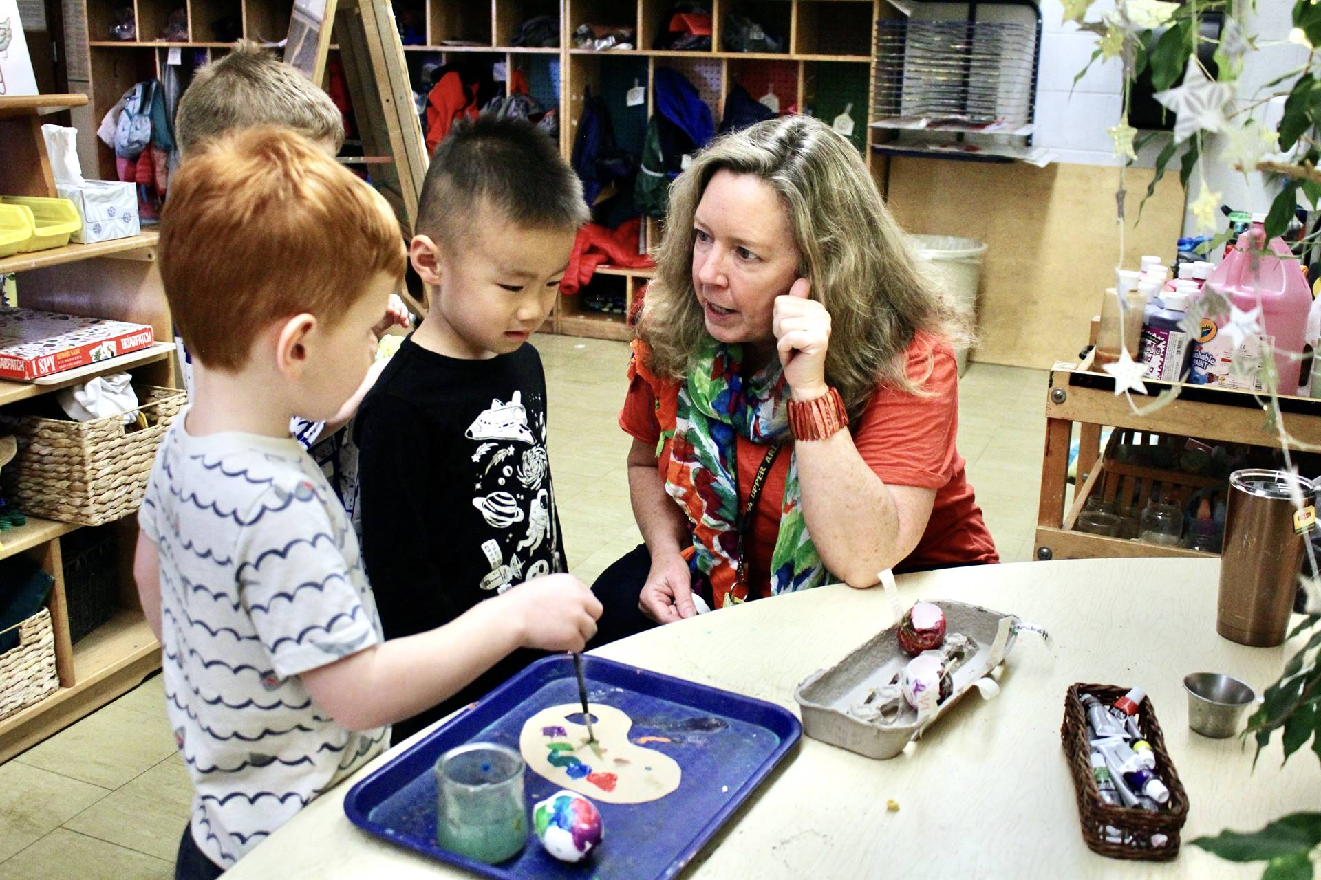 A teacher helping two preschool students with an art activity