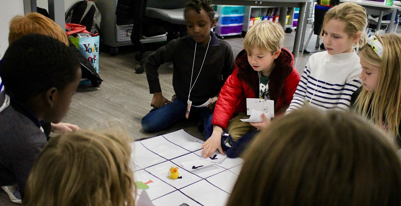 Students doing a hands-on coding activity on a mat on the floor in a classroom