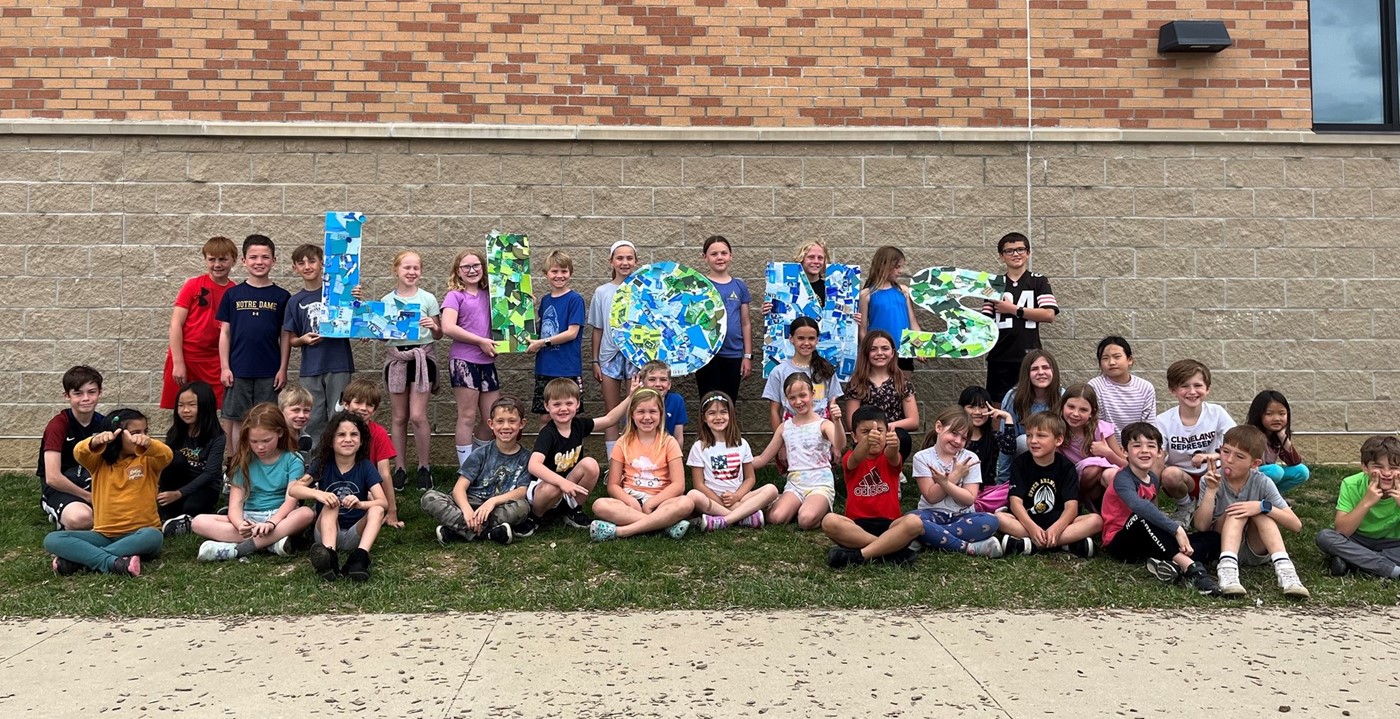 Students posing outside with a &#34;Lions&#34; sign that they made of recycled materials