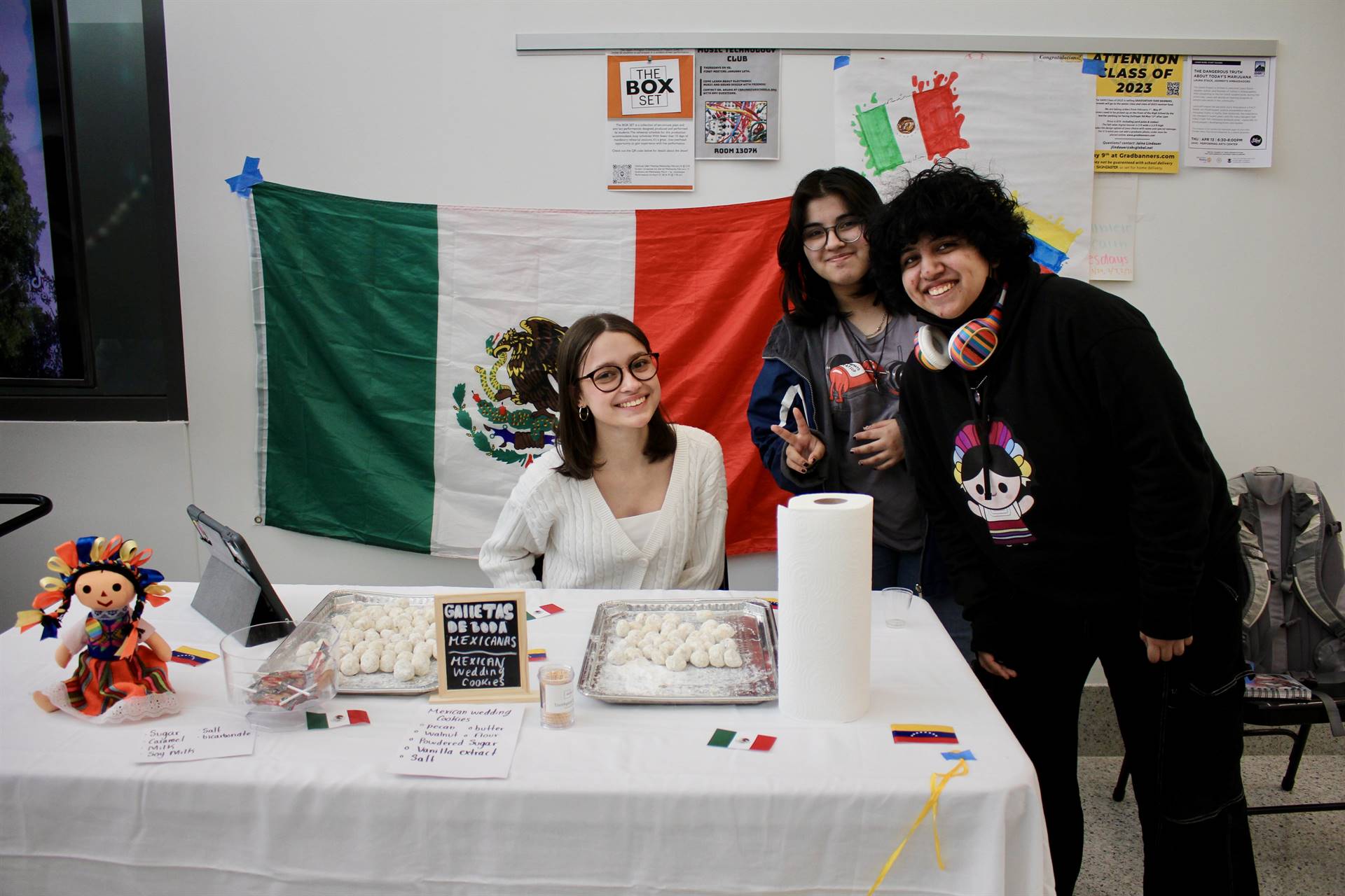 Three students around a table with a Mexican flag hanging behind them